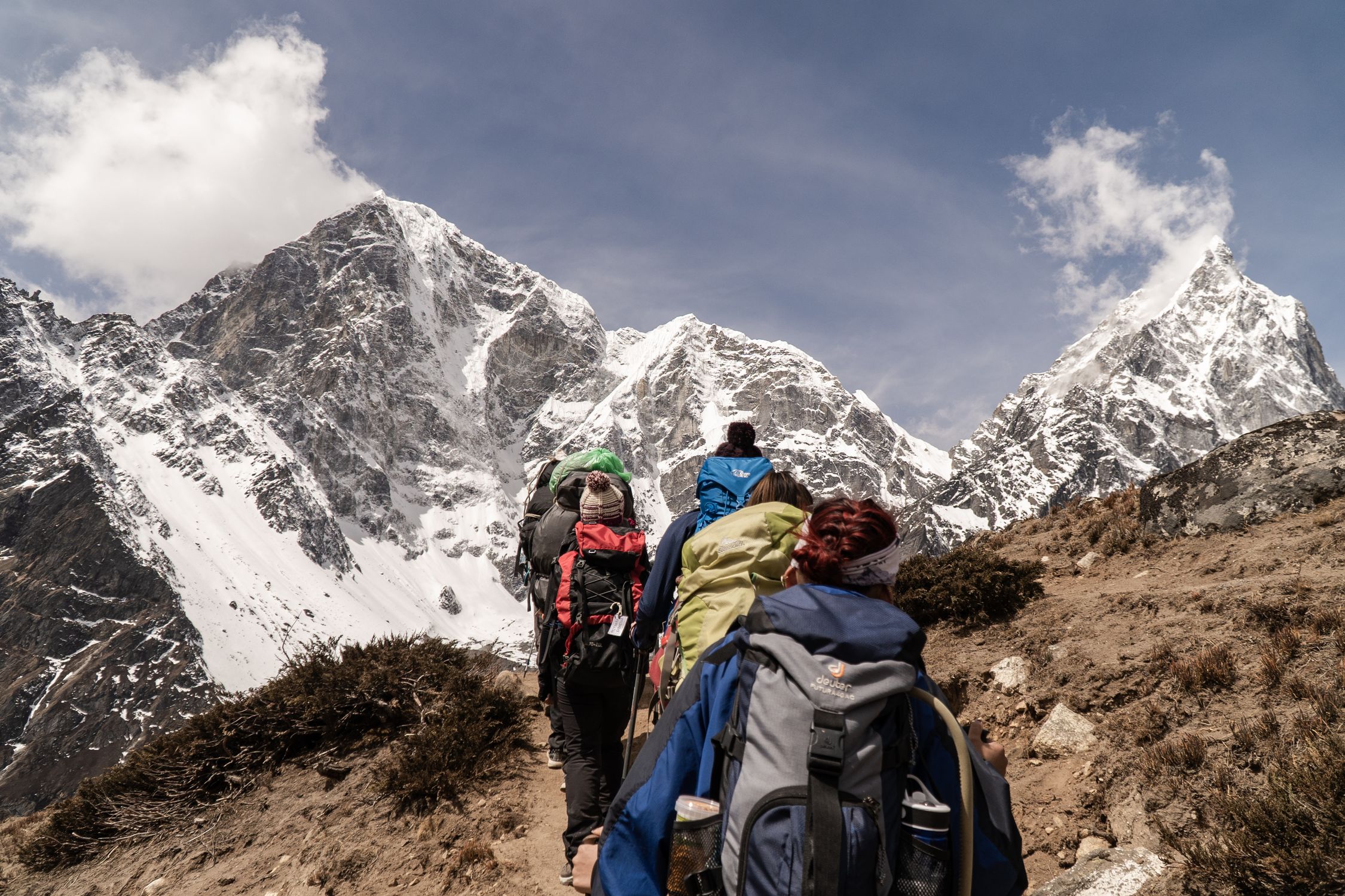 Group of hikers trekking on a sunny day with snow-capped mountains in the background